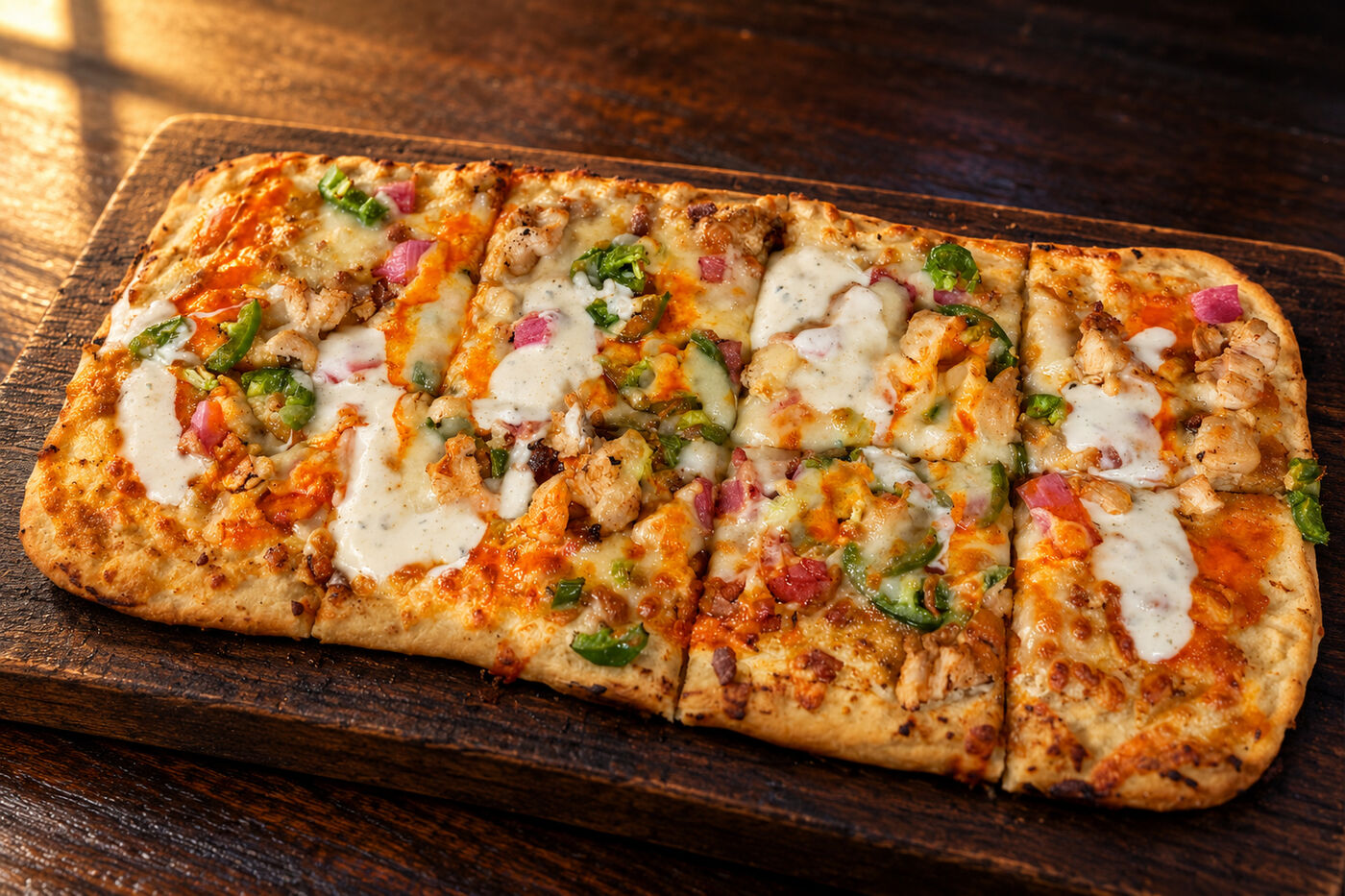 The Hot Chick flatbread with buffalo and ranch drizzle, cut into strips on a board